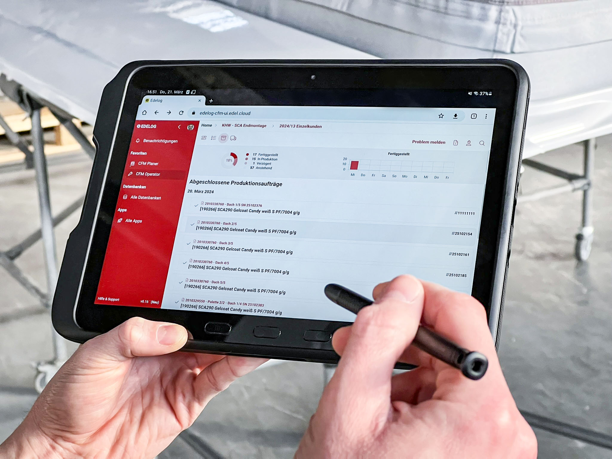 Bild eines Tablets vor dem Hintergrund einer Werkshalle. Auf dem Display sieht man die Benutzeroberfläche der Digitalisierungsplattform EDELOG
